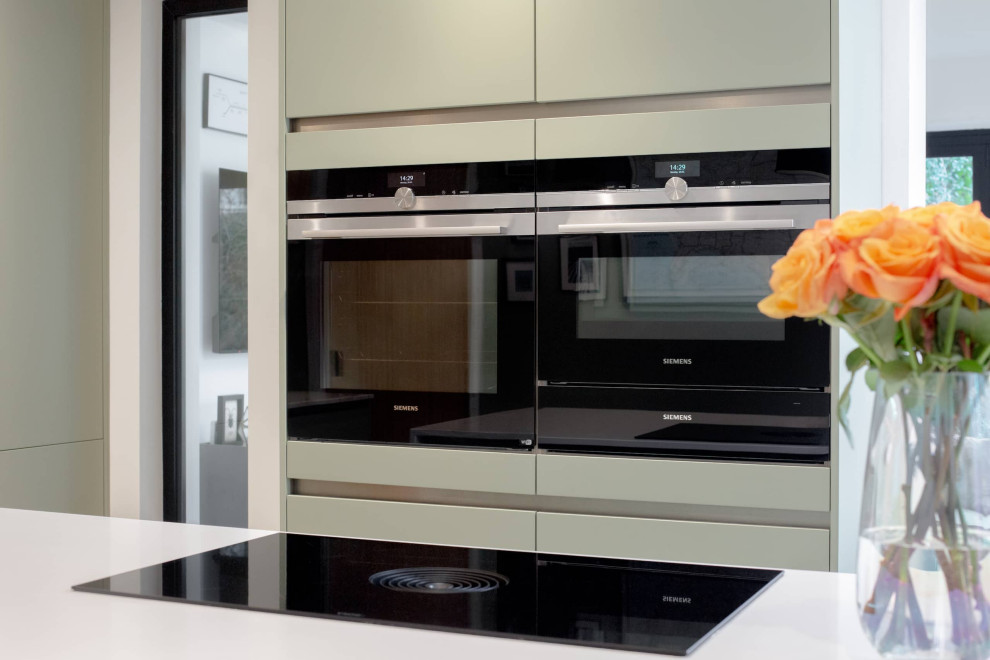 Immagine di una cucina minimal di medie dimensioni con lavello da incasso, ante lisce, ante grigie, top in quarzite, paraspruzzi a specchio, elettrodomestici neri e top bianco