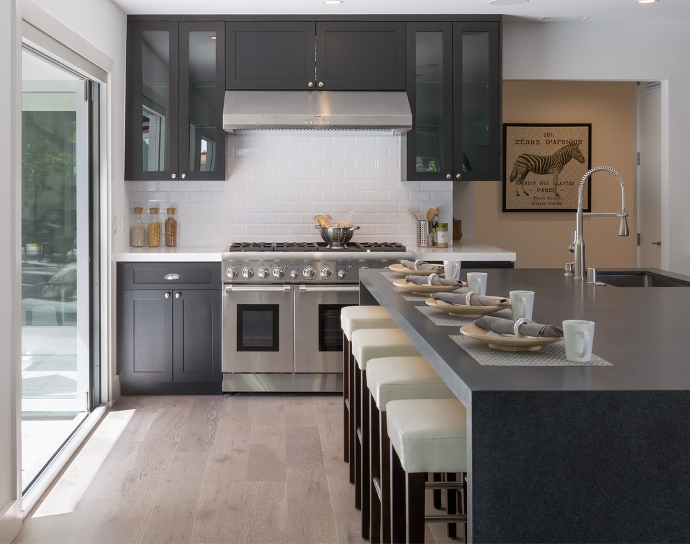 Large contemporary l-shaped open plan kitchen in Los Angeles with an undermount sink, shaker cabinets, black cabinets, quartz benchtops, white splashback, subway tile splashback, stainless steel appliances, ceramic floors, with island and black benchtop.