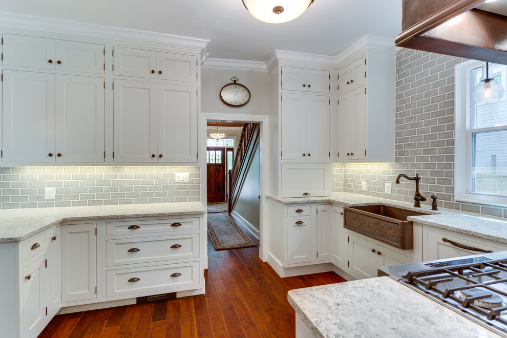 Photo of a mid-sized traditional u-shaped kitchen in DC Metro with a farmhouse sink, white cabinets, quartz benchtops, stainless steel appliances, medium hardwood floors and a peninsula.
