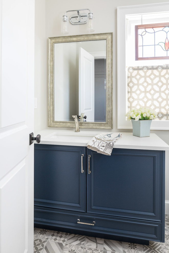 Photo of an expansive country powder room in Toronto with beaded inset cabinets, blue cabinets, a two-piece toilet, multi-coloured tile, grey walls, mosaic tile floors, an undermount sink, engineered quartz benchtops, grey floor and white benchtops.