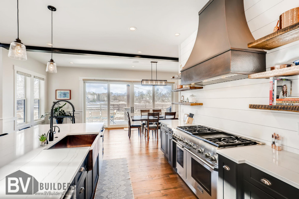 Mid-sized country kitchen in Denver with a farmhouse sink, shaker cabinets, black cabinets, quartz benchtops, white splashback, shiplap splashback, stainless steel appliances, medium hardwood floors, with island, brown floor and white benchtop.