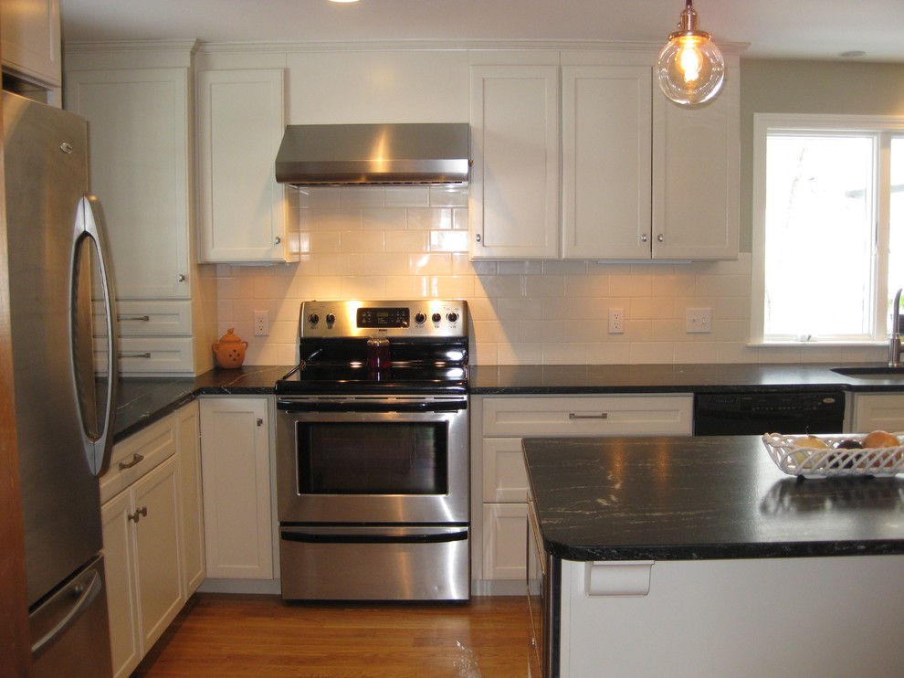 Transitional l-shaped medium tone wood floor eat-in kitchen photo in Boston with an undermount sink, shaker cabinets, white cabinets, quartz countertops, white backsplash, ceramic backsplash, stainless steel appliances, an island and black countertops