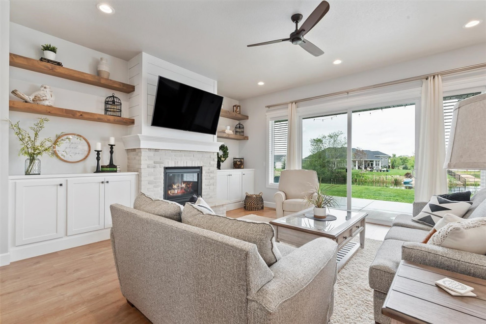 This is an example of a mid-sized traditional open concept living room in Boise with grey walls, laminate floors, a standard fireplace, a brick fireplace surround, a wall-mounted tv and brown floor.