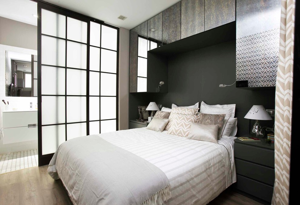 This is an example of a contemporary master bedroom in Madrid with black walls and light hardwood floors.