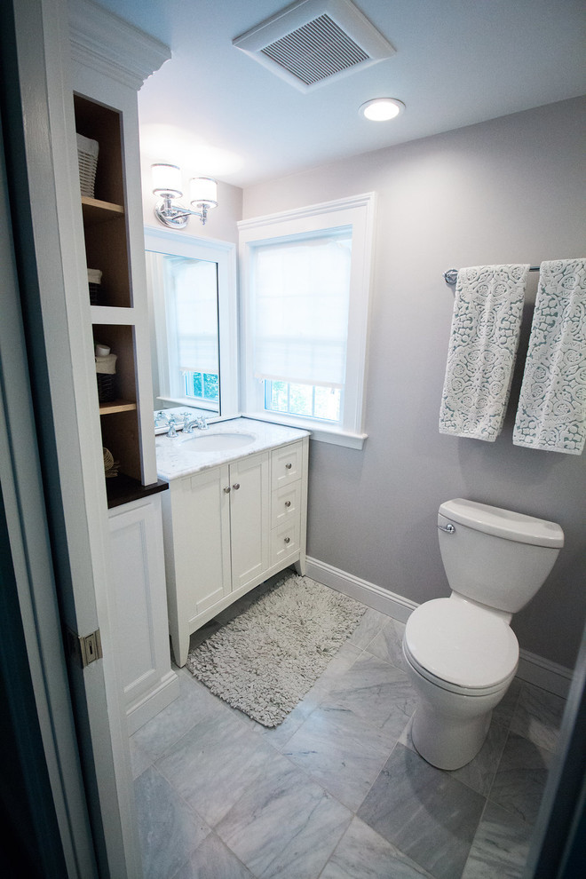 Example of a mid-sized transitional master travertine floor corner shower design in Boston with shaker cabinets, white cabinets, a two-piece toilet, gray walls, an undermount sink and solid surface countertops