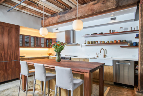 Wabi-sabi kitchen in Canada — reclaimed wood beams, mixed wood cabinets, open shelves with ceramics, apron-front sink, brass faucet, pendant globes, concrete floor