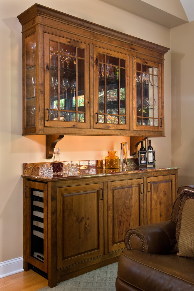 This is an example of a small traditional single-wall home bar in Boston with no sink, raised-panel cabinets, medium wood cabinets, marble benchtops, multi-coloured splashback, marble splashback and medium hardwood floors.
