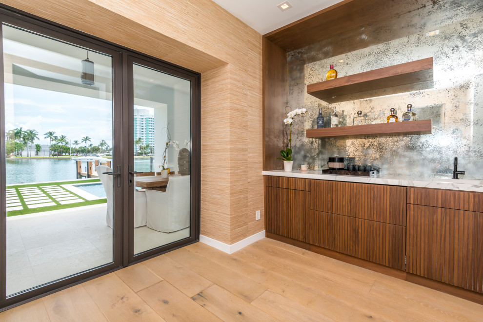 Design ideas for a large midcentury single-wall wet bar in Miami with an integrated sink, beaded inset cabinets, medium wood cabinets, marble benchtops, mirror splashback, medium hardwood floors, brown floor and grey benchtop.