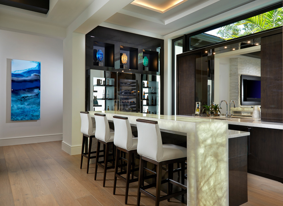 Design ideas for a large transitional l-shaped seated home bar in Miami with an integrated sink, brown splashback, marble splashback, light hardwood floors and white benchtop.