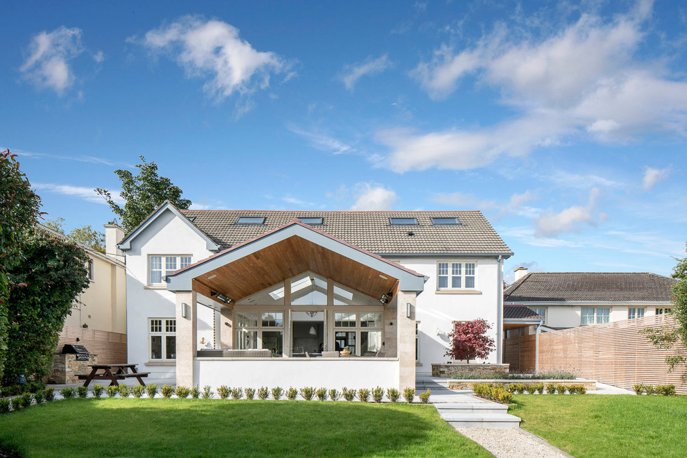 This is an example of a large transitional two-storey stucco white house exterior in Dublin with a tile roof and a gable roof.