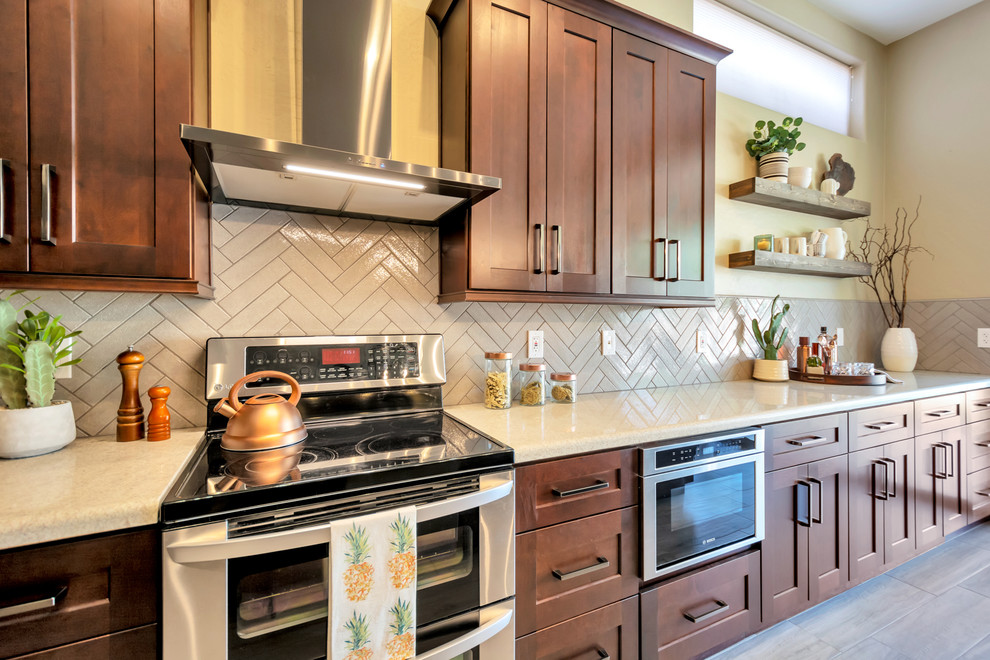 Example of a mid-sized transitional l-shaped porcelain tile and brown floor open concept kitchen design in Phoenix with a single-bowl sink, shaker cabinets, brown cabinets, granite countertops, gray backsplash, brick backsplash, stainless steel appliances, an island and multicolored countertops