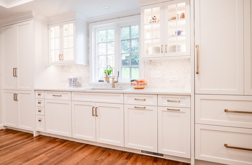 Klassisk inredning av ett vit vitt kök och matrum, med en undermonterad diskho, vita skåp, bänkskiva i kvartsit, mellanmörkt trägolv, brunt golv, stänkskydd i stenkakel och flerfärgad stänkskydd