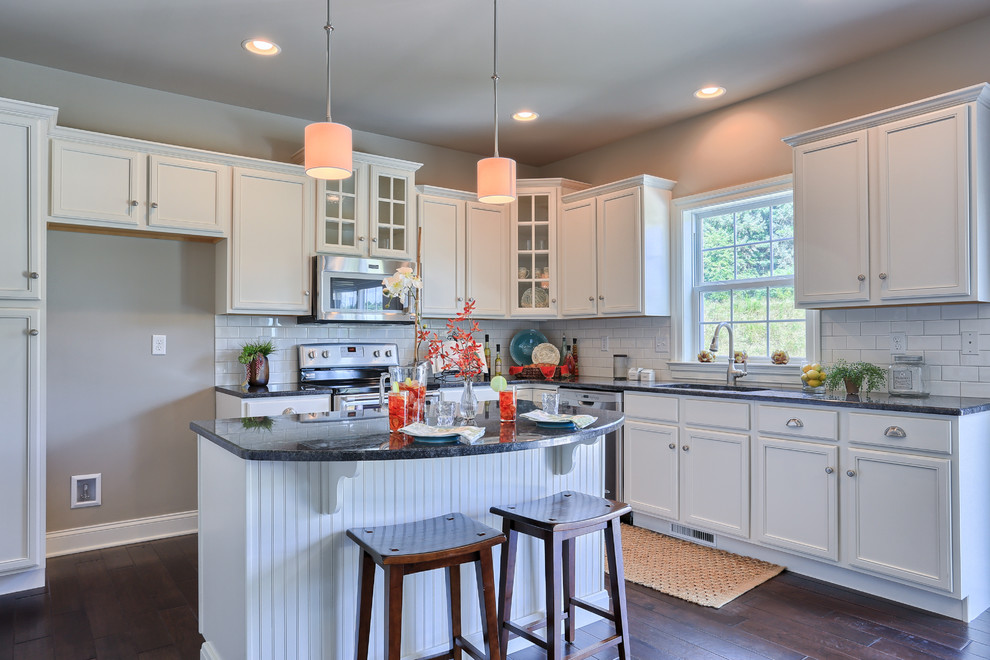 Example of a large transitional l-shaped dark wood floor eat-in kitchen design with recessed-panel cabinets, white cabinets, granite countertops, white backsplash, ceramic backsplash, stainless steel appliances and an island