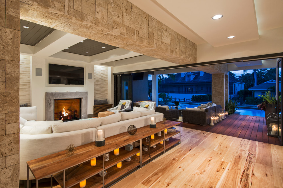 Design ideas for a large modern open concept family room in Miami with white walls, light hardwood floors, a standard fireplace, a stone fireplace surround and a wall-mounted tv.