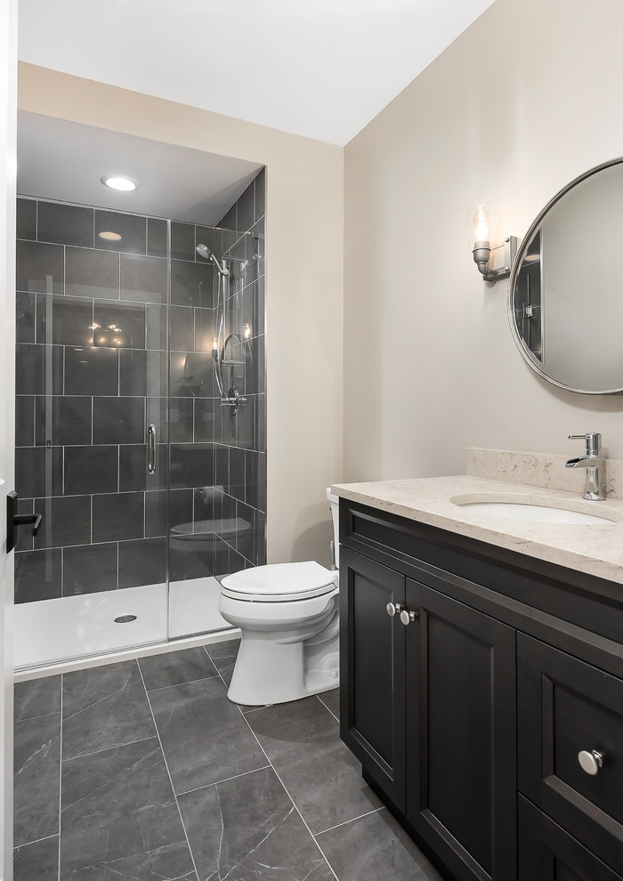 Inspiration for a mid-sized transitional 3/4 bathroom in Chicago with recessed-panel cabinets, brown cabinets, beige walls, ceramic floors, an undermount sink, engineered quartz benchtops, grey floor, beige benchtops, an alcove shower, a two-piece toilet and a hinged shower door.