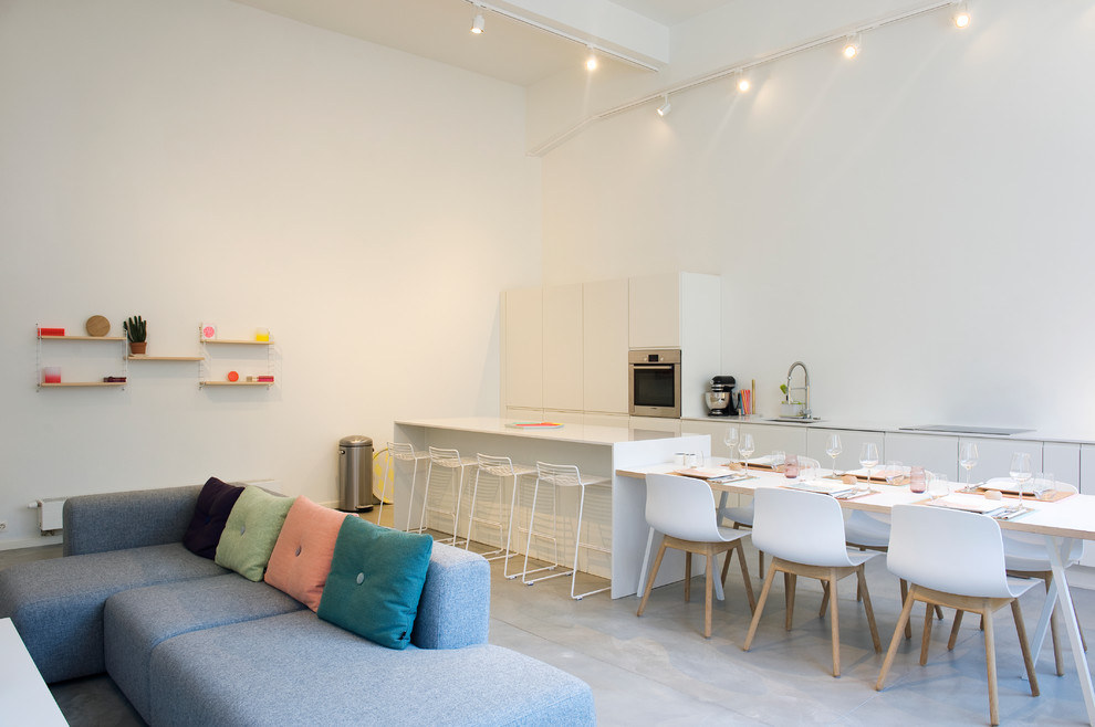This is an example of an industrial open plan kitchen in Brussels with flat-panel cabinets, white cabinets, stainless steel appliances, concrete floors and with island.