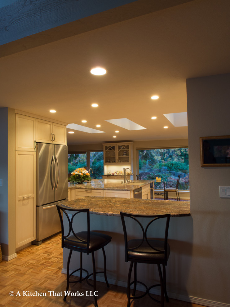 Large transitional u-shaped medium tone wood floor and brown floor eat-in kitchen photo in Seattle with an undermount sink, recessed-panel cabinets, white cabinets, granite countertops, stone slab backsplash, stainless steel appliances, an island, brown backsplash and brown countertops