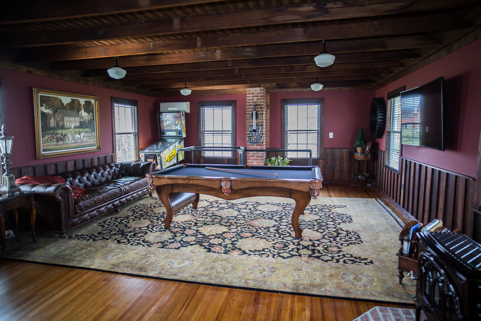 This is an example of a mid-sized country open concept family room in DC Metro with medium hardwood floors, brown floor, a game room, red walls and a wall-mounted tv.