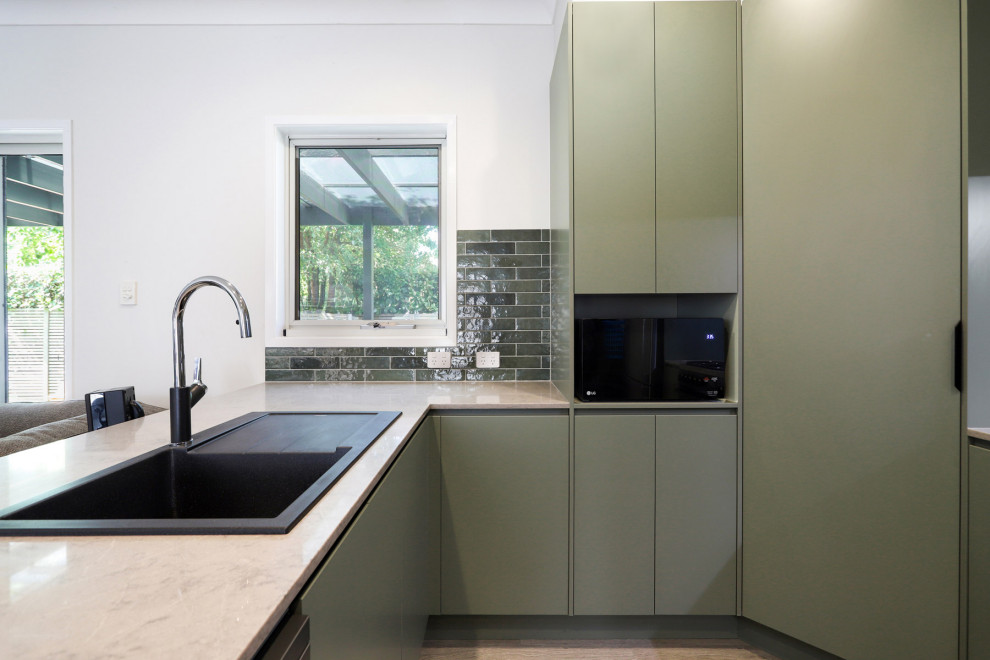 Mid-sized contemporary u-shaped open plan kitchen in Sydney with a single-bowl sink, green cabinets, quartz benchtops, green splashback, ceramic splashback, stainless steel appliances and laminate floors.