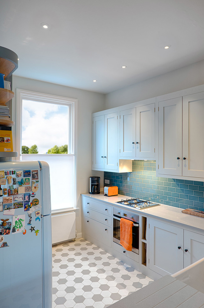 Photo of a mid-sized traditional u-shaped open plan kitchen in Hampshire with a farmhouse sink, shaker cabinets, grey cabinets, limestone benchtops, blue splashback, ceramic splashback, stainless steel appliances, porcelain floors, no island and grey floor.