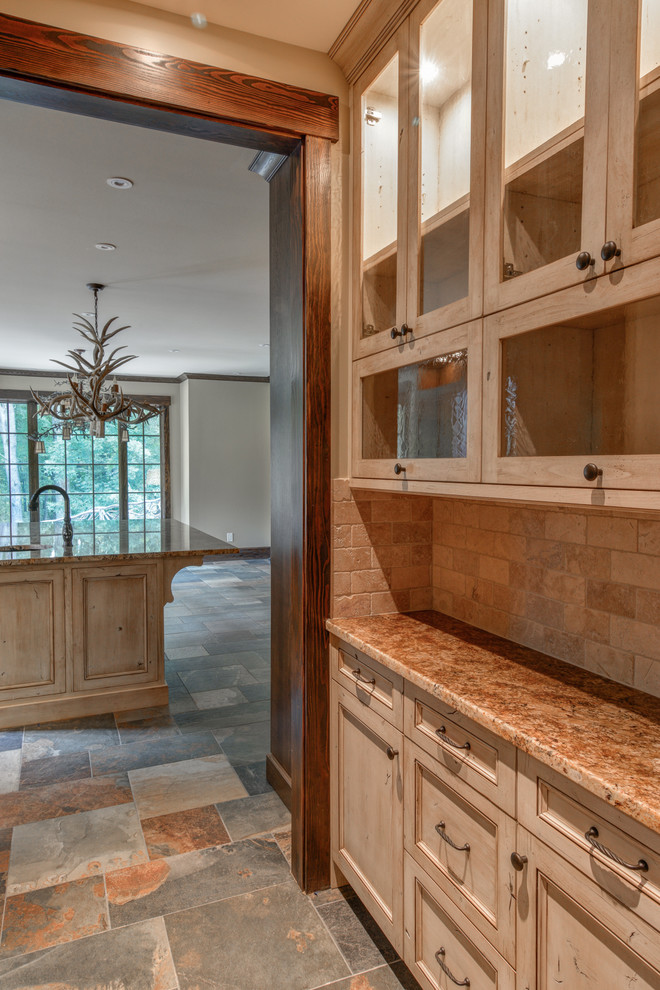 Large mountain style l-shaped slate floor and gray floor enclosed kitchen photo with an undermount sink, recessed-panel cabinets, dark wood cabinets, granite countertops, beige backsplash, stone tile backsplash, paneled appliances, a peninsula and brown countertops