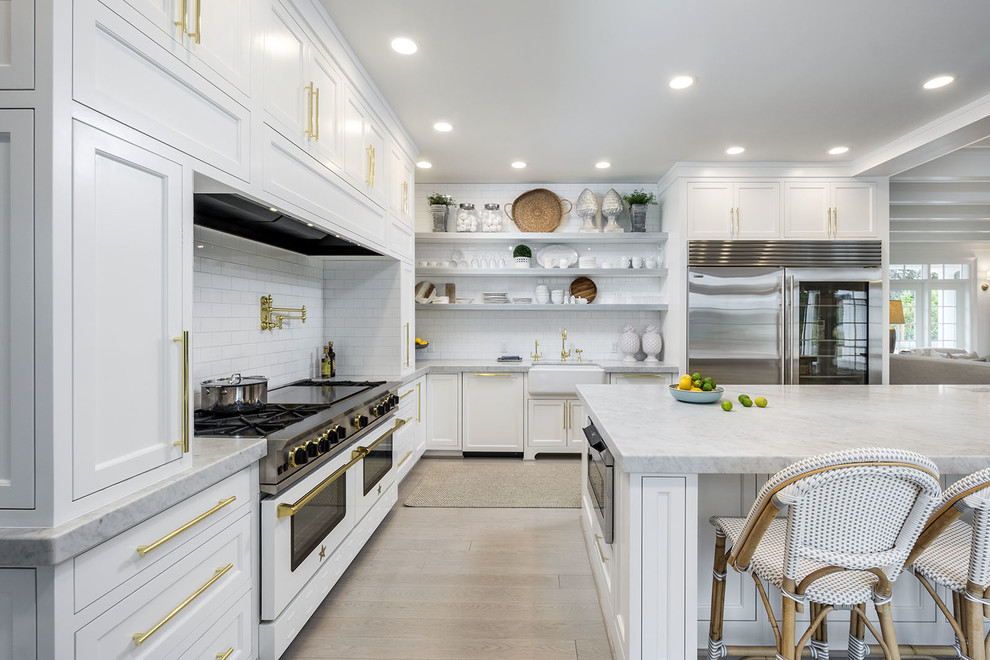 This is an example of a country l-shaped open plan kitchen in Portland with white cabinets, a farmhouse sink, recessed-panel cabinets, white splashback, subway tile splashback, stainless steel appliances, light hardwood floors, with island and beige floor.