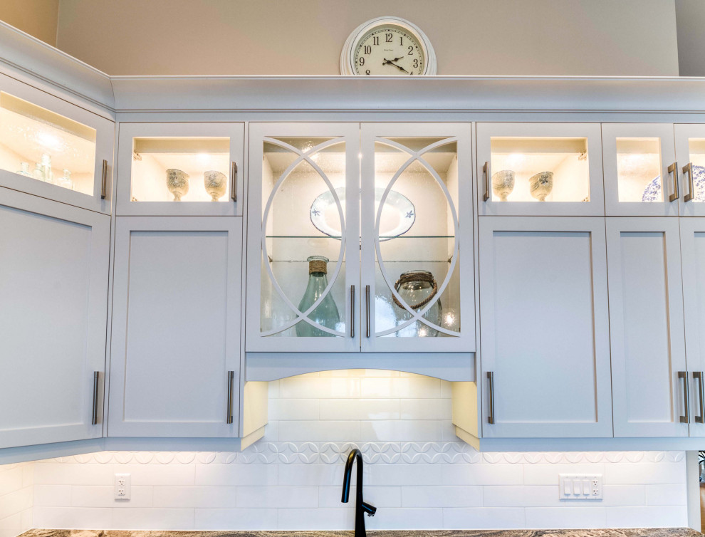 Large transitional l-shaped light wood floor and brown floor eat-in kitchen photo with a farmhouse sink, shaker cabinets, white cabinets, granite countertops, ceramic backsplash, stainless steel appliances and an island