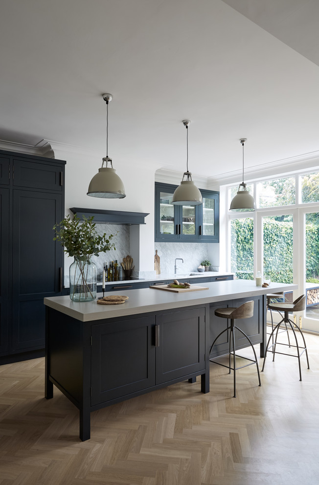 Large contemporary galley eat-in kitchen in London with shaker cabinets, blue cabinets, concrete benchtops, white splashback, marble splashback and with island.