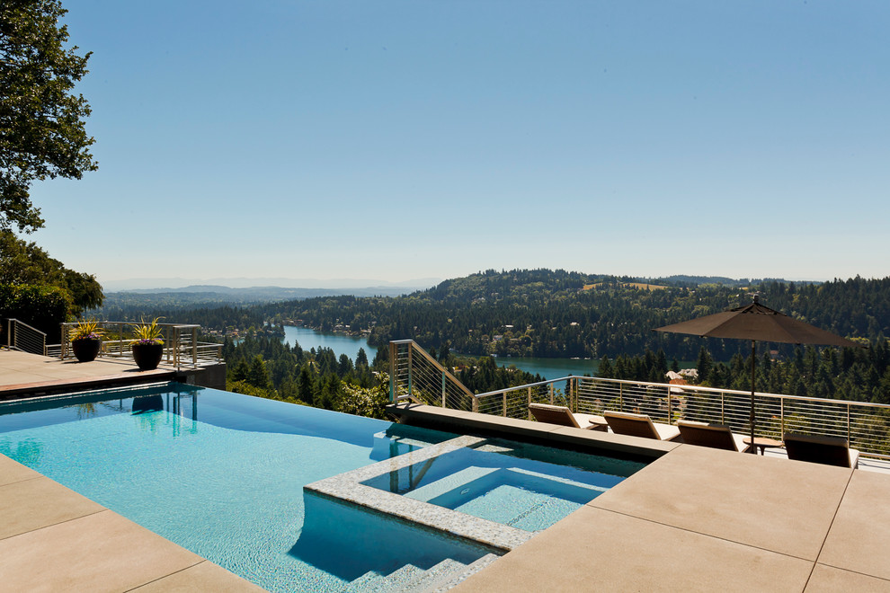 This is an example of a mid-sized contemporary backyard l-shaped infinity pool in Portland with a hot tub and concrete slab.