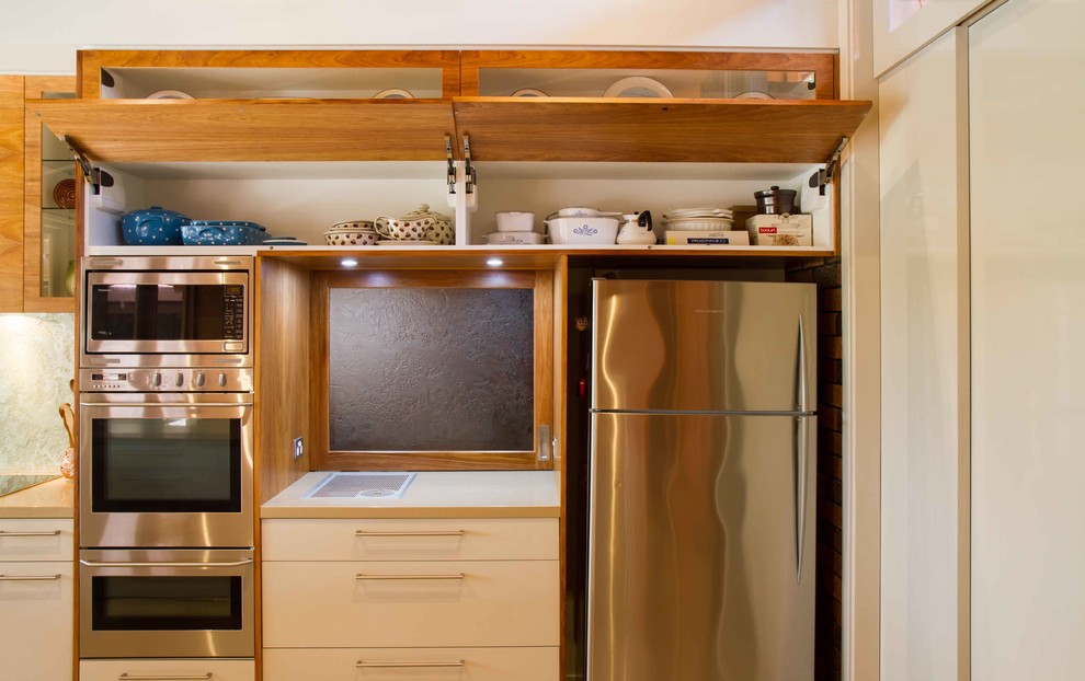 This is an example of a large midcentury u-shaped eat-in kitchen in Melbourne with flat-panel cabinets, quartz benchtops, glass sheet splashback, stainless steel appliances and a peninsula.