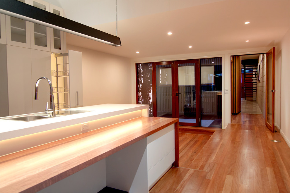 Large contemporary galley open plan kitchen in Other with a double-bowl sink, glass-front cabinets, white cabinets, quartz benchtops, brown splashback, glass sheet splashback, stainless steel appliances, dark hardwood floors, with island and brown floor.