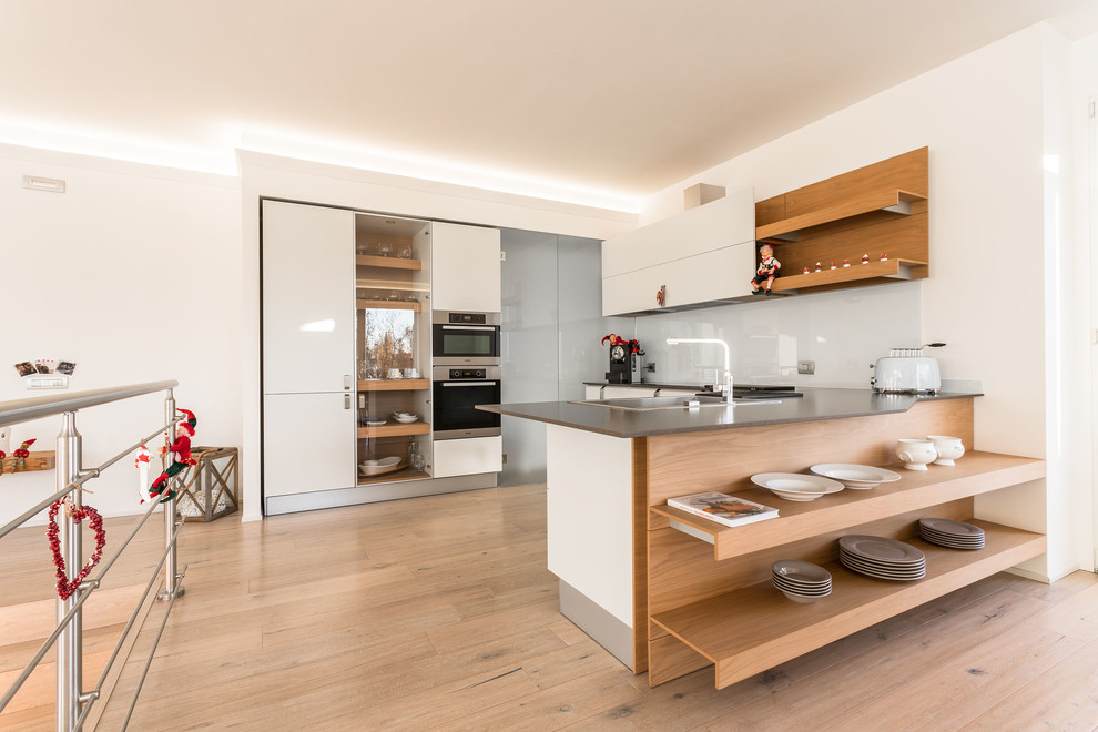 Contemporary u-shaped kitchen in Other with a drop-in sink, open cabinets, white cabinets, white splashback, stainless steel appliances, medium hardwood floors, brown floor and grey benchtop.