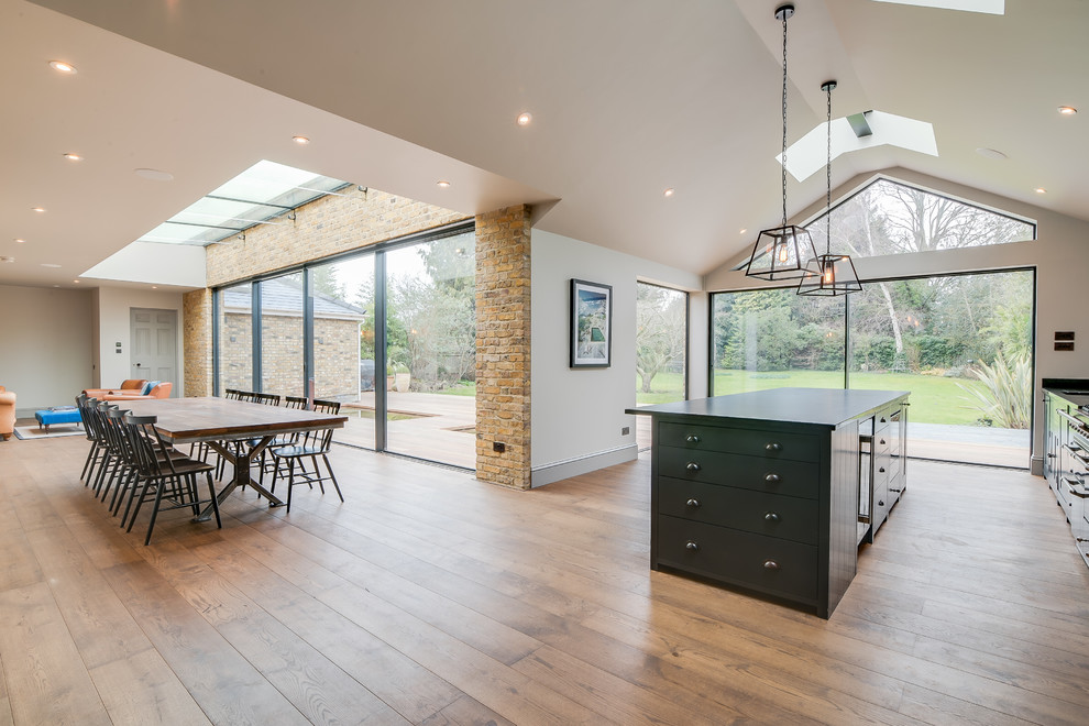Large contemporary galley eat-in kitchen in Surrey with a drop-in sink, shaker cabinets, blue cabinets, white splashback, ceramic splashback, stainless steel appliances, medium hardwood floors, with island, brown floor and black benchtop.