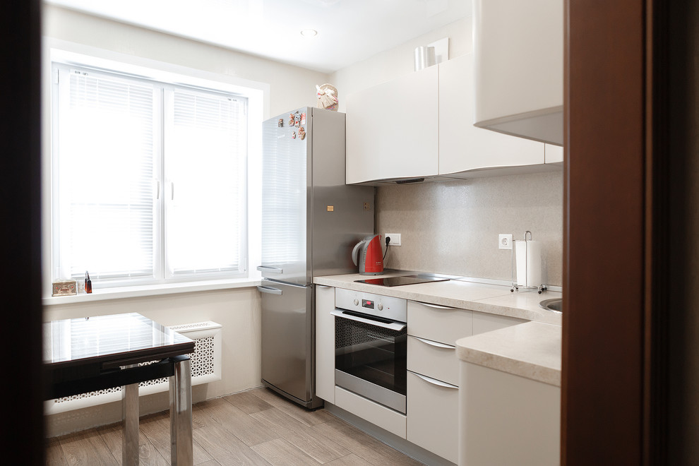 This is an example of a small contemporary l-shaped kitchen in Moscow with an undermount sink, beige cabinets, granite benchtops, beige splashback, ceramic splashback, stainless steel appliances, laminate floors, with island, brown floor and beige benchtop.