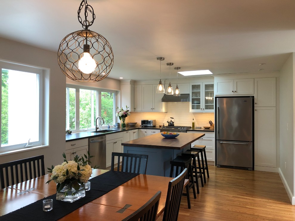 Inspiration for a mid-sized transitional l-shaped medium tone wood floor and brown floor open concept kitchen remodel in Boston with a single-bowl sink, shaker cabinets, white cabinets, granite countertops, white backsplash, window backsplash, stainless steel appliances, an island and black countertops