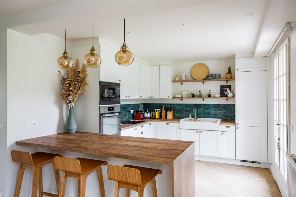 Bild på ett minimalistiskt brun brunt u-kök, med en nedsänkt diskho, luckor med infälld panel, vita skåp, träbänkskiva, grönt stänkskydd, integrerade vitvaror, en halv köksö och beiget golv