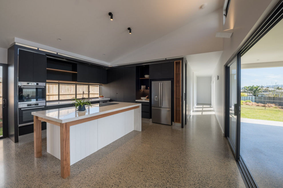 This is an example of a mid-sized modern l-shaped open plan kitchen in Brisbane with an undermount sink, flat-panel cabinets, quartz benchtops, window splashback, stainless steel appliances, concrete floors, with island, grey floor, white benchtop, vaulted and black cabinets.