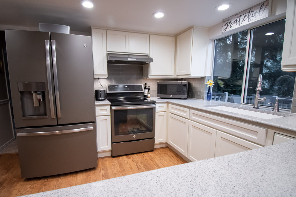 Example of a transitional u-shaped medium tone wood floor open concept kitchen design in Seattle with an undermount sink, shaker cabinets, white cabinets, quartz countertops, gray backsplash, glass tile backsplash, stainless steel appliances, a peninsula and multicolored countertops
