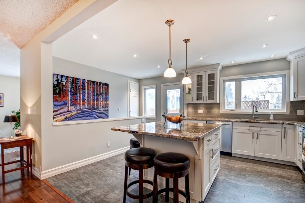 Example of a mid-sized transitional l-shaped vinyl floor eat-in kitchen design in Calgary with an undermount sink, shaker cabinets, white cabinets, granite countertops, gray backsplash, subway tile backsplash, stainless steel appliances and an island