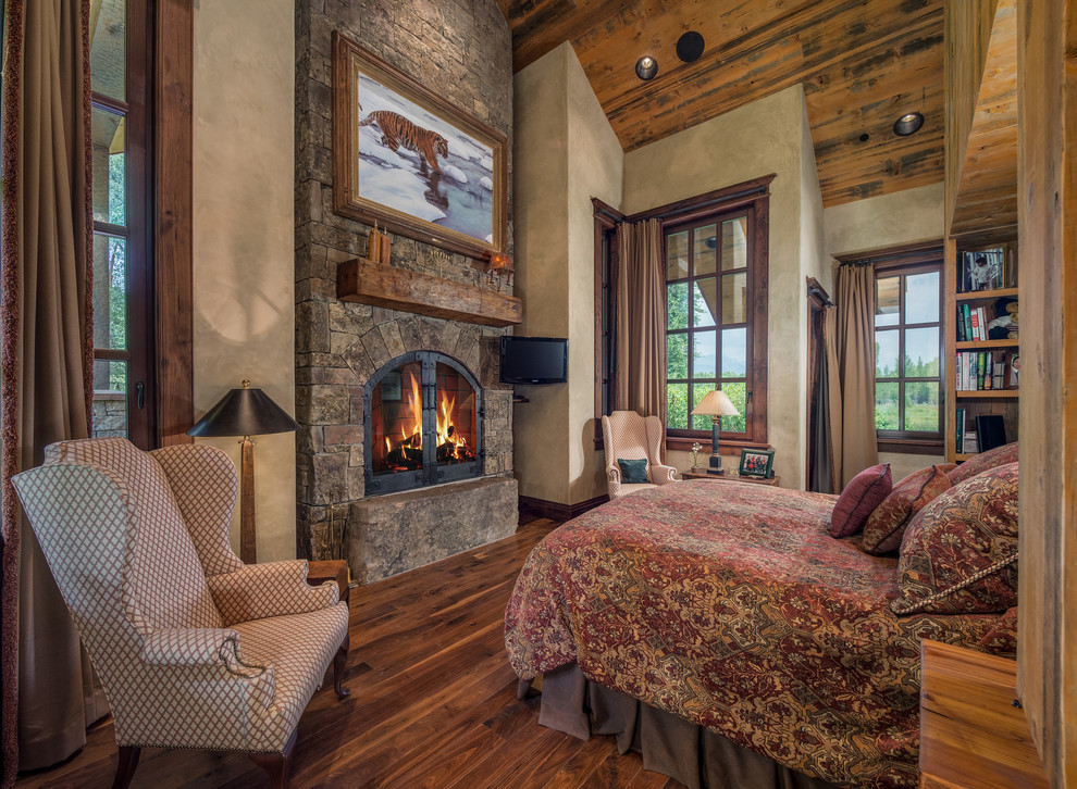Country bedroom in Other with grey walls, medium hardwood floors, a standard fireplace, a stone fireplace surround and brown floor.