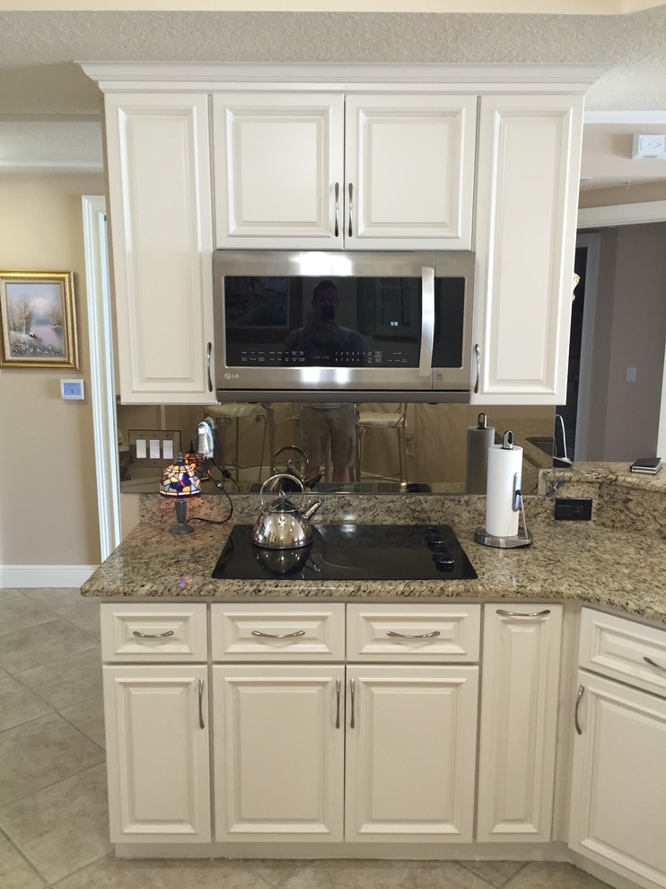 This is an example of a mid-sized beach style l-shaped eat-in kitchen in Orlando with an undermount sink, raised-panel cabinets, white cabinets, granite benchtops, beige splashback, stone slab splashback, stainless steel appliances, porcelain floors and no island.