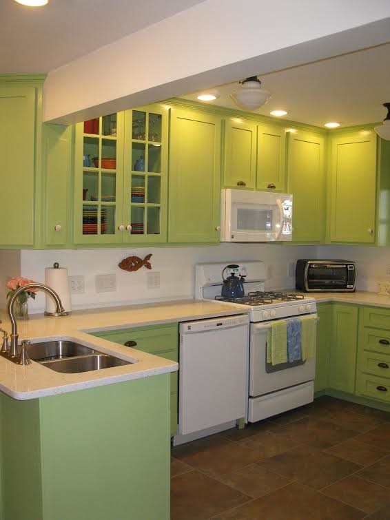Photo of a small traditional u-shaped eat-in kitchen in New York with a double-bowl sink, shaker cabinets, green cabinets, solid surface benchtops, white splashback, white appliances, ceramic floors and a peninsula.
