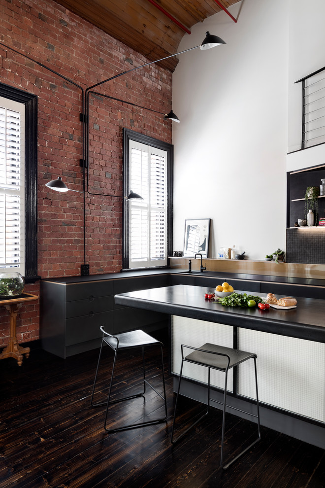 Photo of an industrial l-shaped kitchen in Melbourne with an undermount sink, flat-panel cabinets, black cabinets, black splashback, mosaic tile splashback, dark hardwood floors, with island, brown floor and black benchtop.