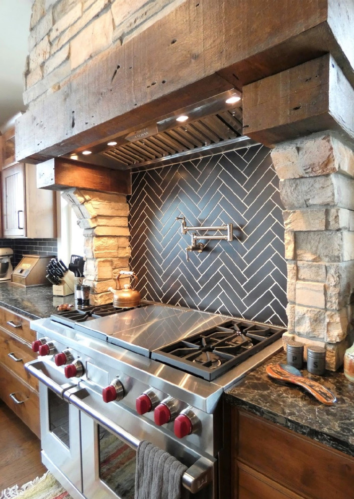Inspiration for a rustic kitchen remodel in Grand Rapids with a farmhouse sink, recessed-panel cabinets, dark wood cabinets, quartz countertops, black backsplash, travertine backsplash, stainless steel appliances, an island and brown countertops
