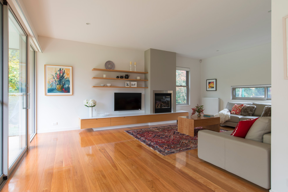Large contemporary open concept family room in Wollongong with a wall-mounted tv, white walls, light hardwood floors, a wood stove and a brick fireplace surround.