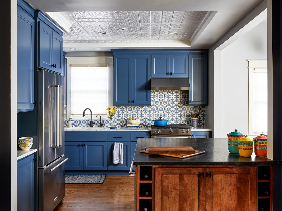 Imagen de cocina comedor clásica de tamaño medio con puertas de armario azules, salpicadero azul, electrodomésticos de acero inoxidable, suelo de madera en tonos medios y una isla