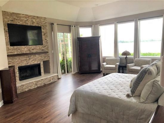 Inspiration for an expansive transitional master bedroom in Orlando with grey walls, vinyl floors, a standard fireplace, a stone fireplace surround and brown floor.