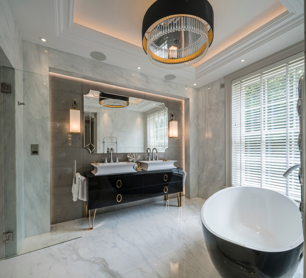 Photo of a transitional bathroom in London with black cabinets, a freestanding tub, white tile, marble floors, a vessel sink, a hinged shower door and flat-panel cabinets.