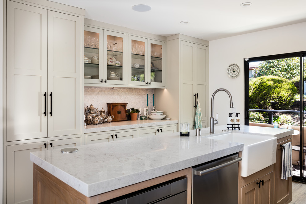 This is an example of a mid-sized transitional galley eat-in kitchen in Los Angeles with shaker cabinets, beige cabinets, granite benchtops, beige splashback, ceramic splashback, stainless steel appliances, with island, beige benchtop, a farmhouse sink, light hardwood floors and grey floor.