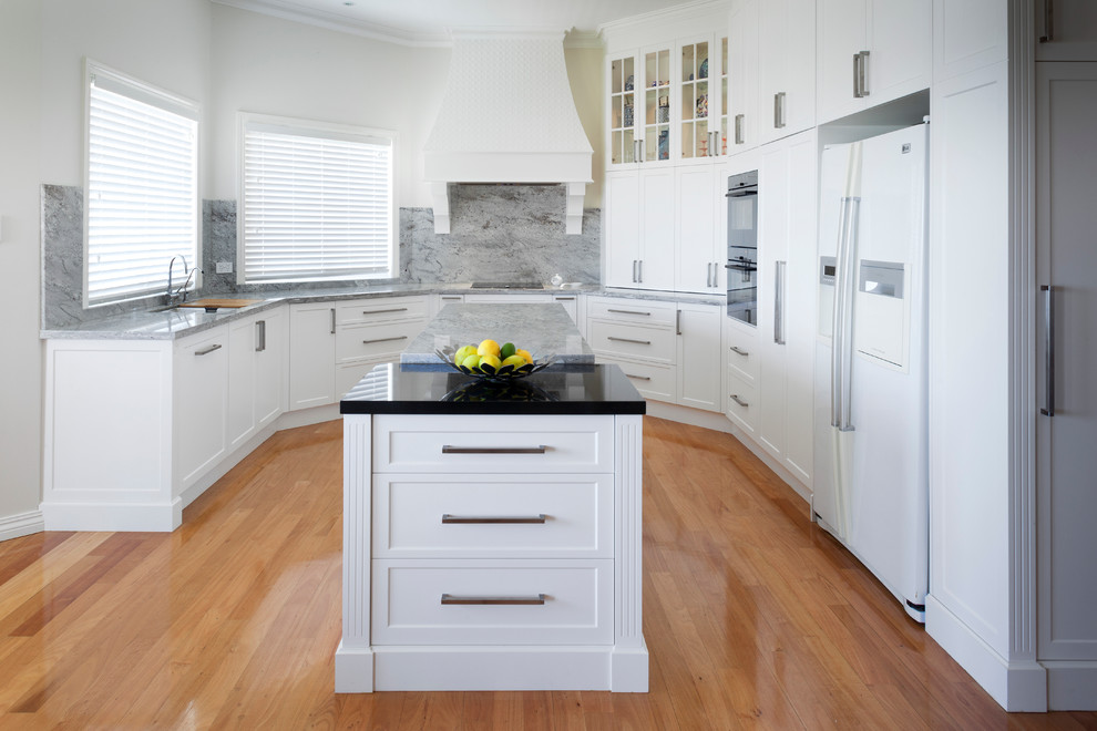 This is an example of a traditional kitchen in Perth with recessed-panel cabinets, white cabinets, granite benchtops, grey splashback, stone slab splashback, multiple islands, grey benchtop and medium hardwood floors.